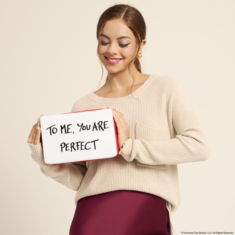 Woman wearing a white sweater with a red silk skirt, holding the Loungefly Love Actually crossbody bag. She stands against a cream-colored background. 